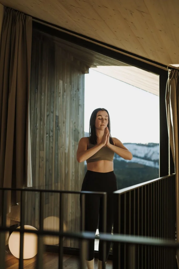 Vrouw mediteert met gesloten ogen bij groot raam met uitzicht op bergen