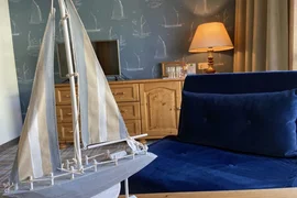 Model zeilboot op tafel bij blauwe fauteuil en houten kast