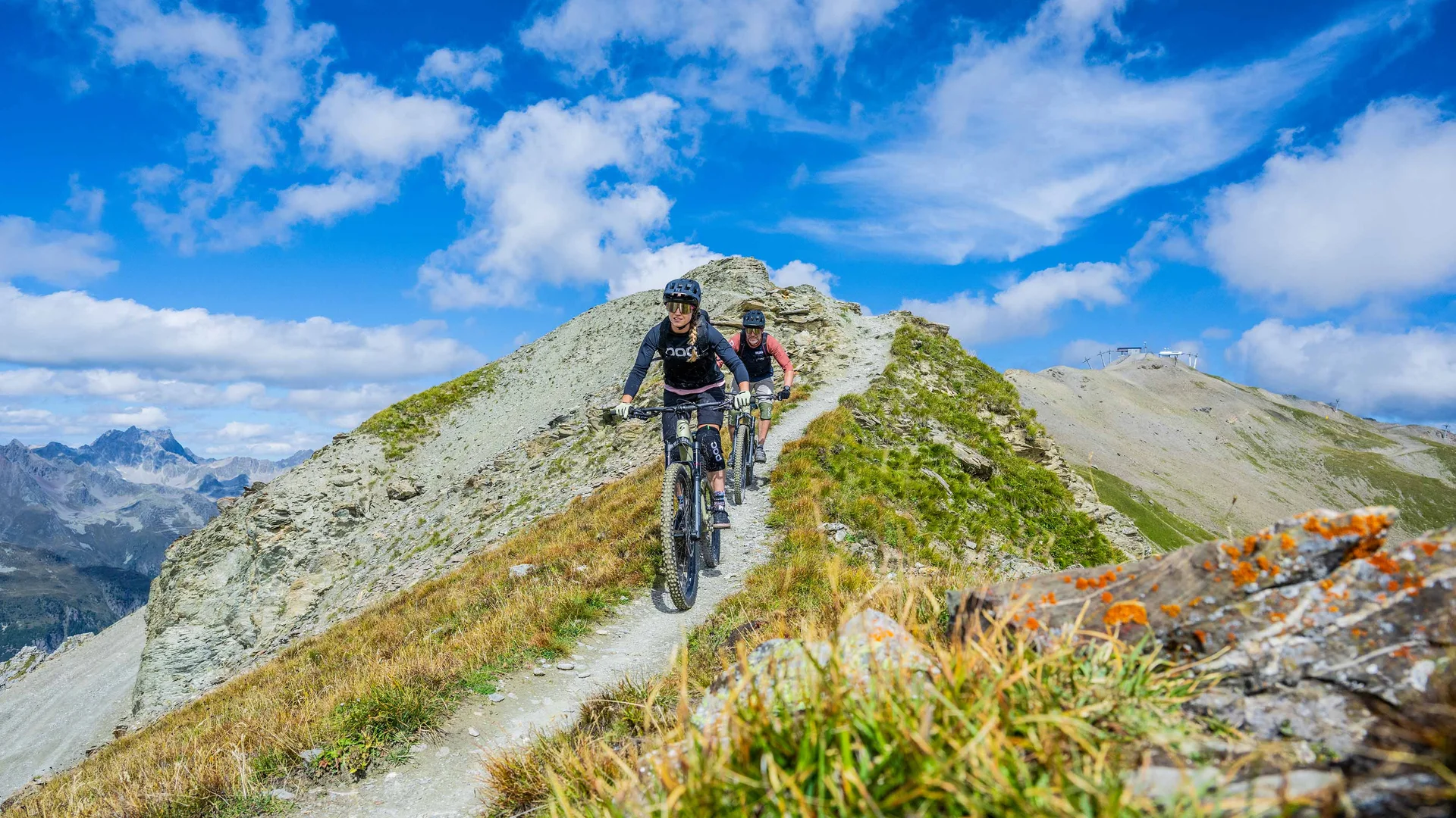 Zwei Mountainbiker fahren auf schmalem Gebirgspfad bei klarem Himmel