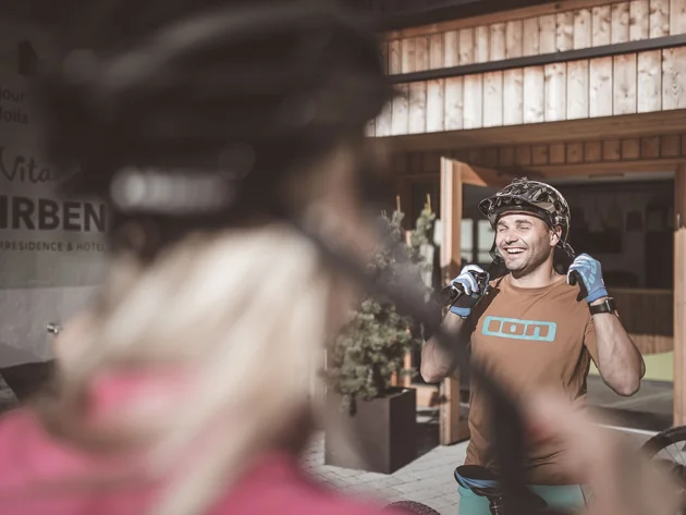 Was steckt hinter dem Umweltengagement von Bikehotels? © Manuel Kottersteger Mann mit Fahrradhelm und Handschuhen lacht vor einem Hotel mit Holzeingang