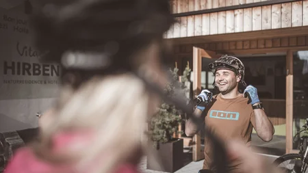 Was steckt hinter dem Umweltengagement von Bikehotels? © Manuel Kottersteger Mann mit Fahrradhelm und Handschuhen lacht vor einem Hotel mit Holzeingang
