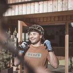 Man wearing bike helmet and gloves smiling in front of hotel with wooden entrance