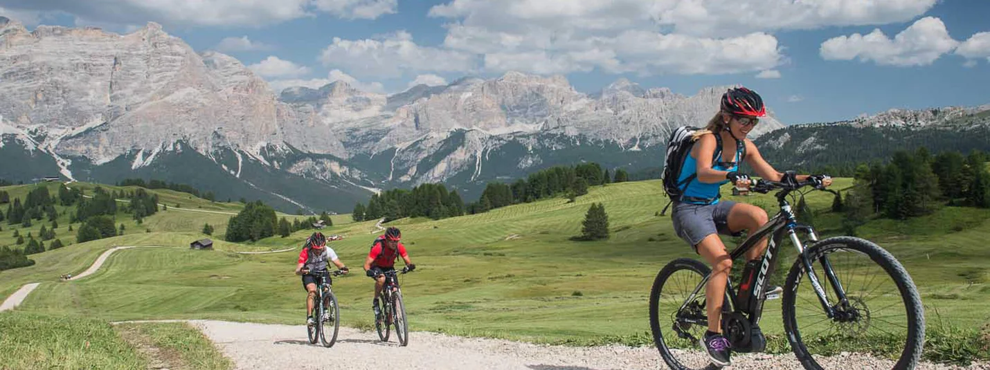 Drei Fahrradfahrer auf Schotterweg vor Bergkulisse bei sonnigem Wetter