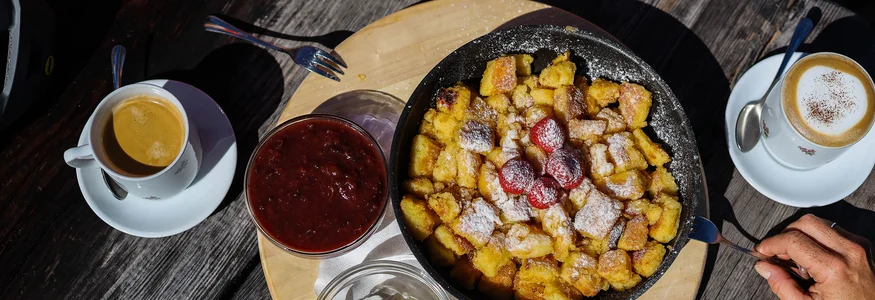 Kaiserschmarrn mit Erdbeeren, Sahne, Marmelade und Kaffee auf Holz-Tisch