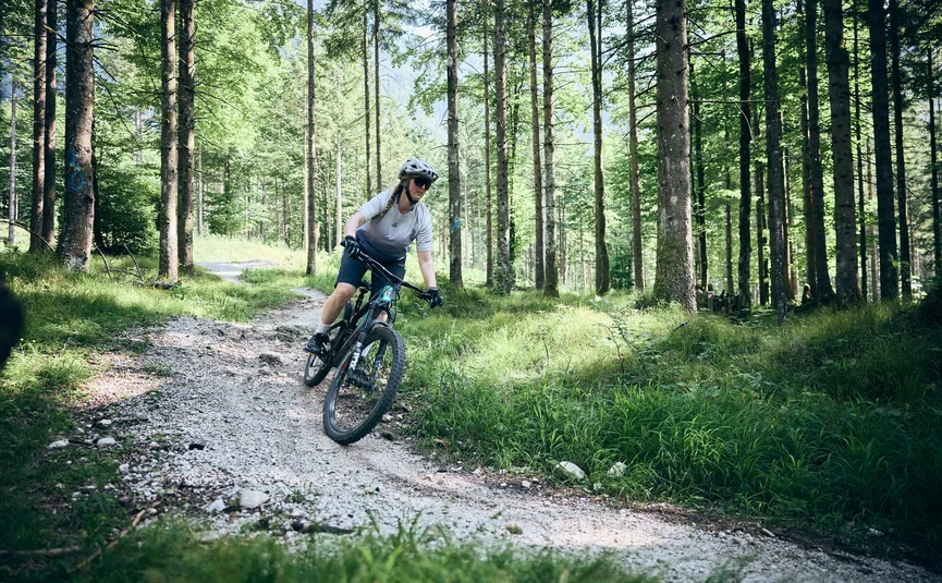 Woman mountain biking on forest trail wearing helmet and sunglasses