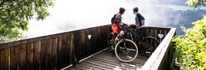 Zwei Mountainbiker auf einer Aussichtsplattform schauen ins neblige Tal