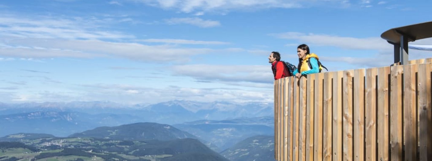 Two people looking from wooden viewpoint over mountain landscape