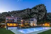 Hotel mit beleuchtetem Pool am Abend vor einem großen Felsen