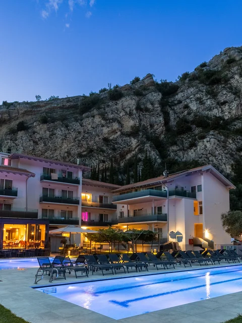 Hotel mit beleuchtetem Pool am Abend vor einem großen Felsen