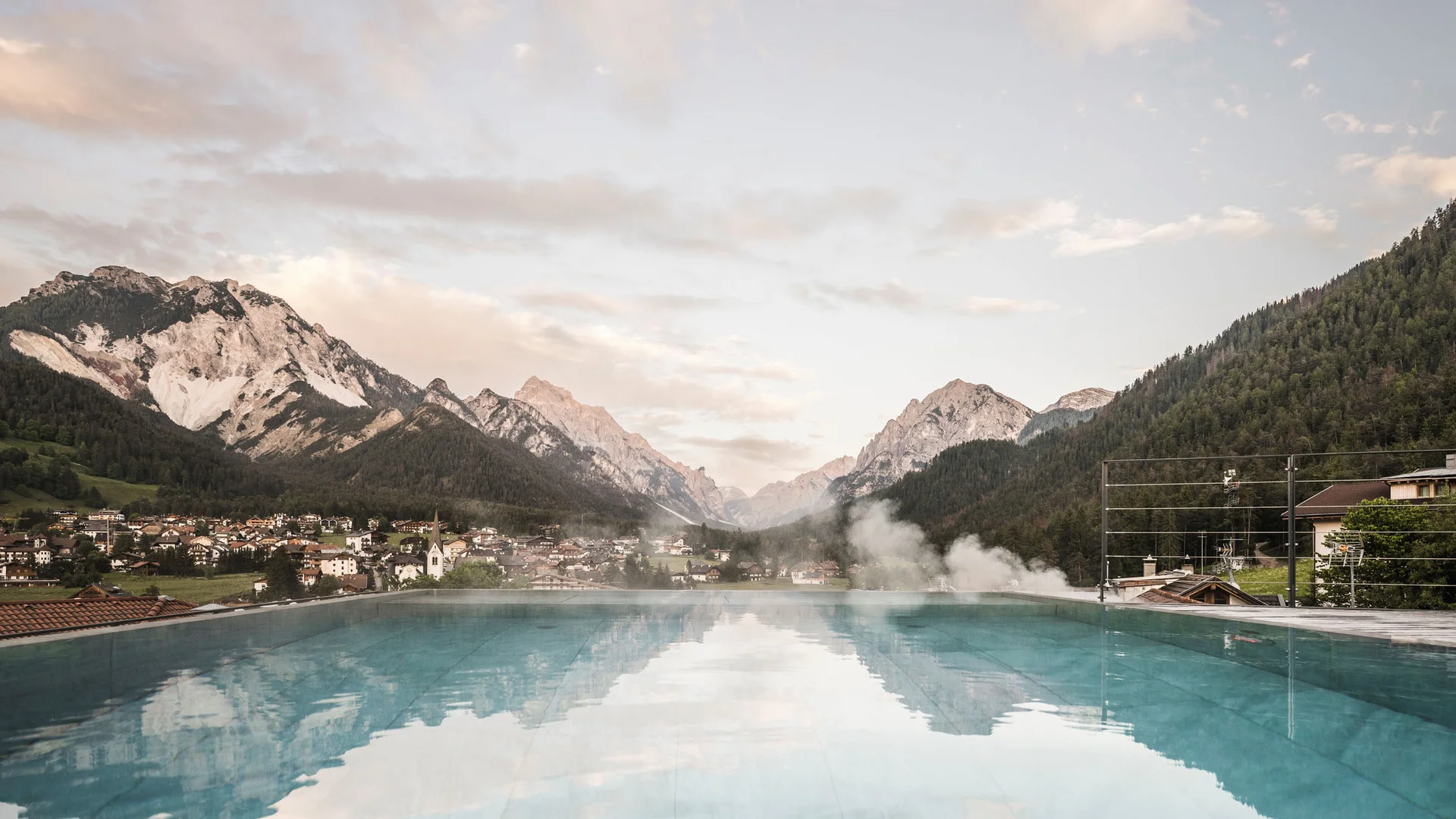 Infinity-Pool mit Blick auf Alpen und Dorf im Tal