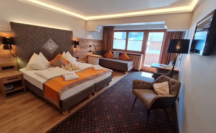 Gemütliches Hotelzimmer mit Doppelbett, Sofa, Sessel und Balkonfenster