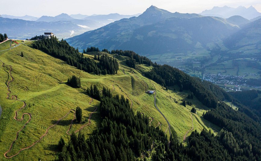 Hahnenkamm Trail © TVB Kitzbüheler Alpen-Brixental, Fotograf Andreas Meyer Grüne Alpenhügel mit Wanderwegen und Bergen im Hintergrund bei Sonnenlicht