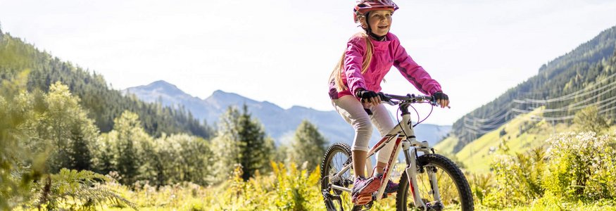 Mädchen fährt Mountainbike über Holzhindernis in Berglandschaft