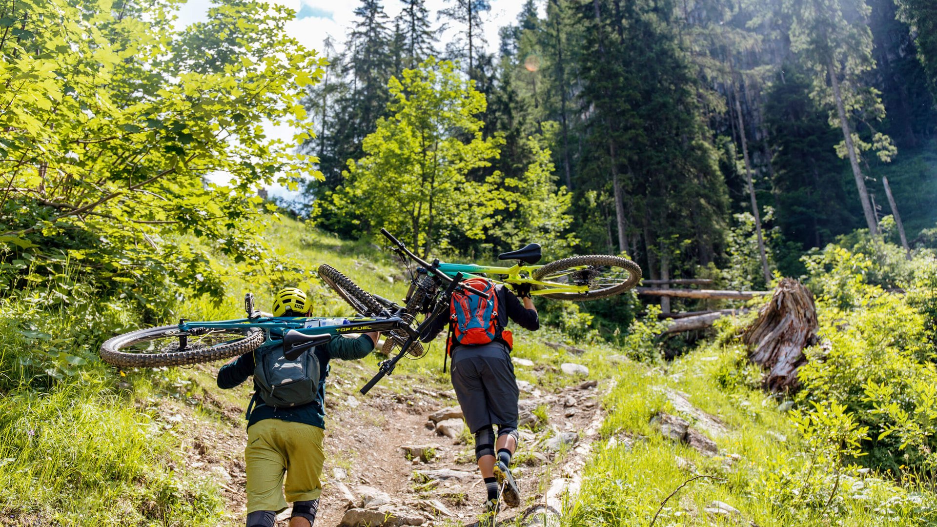Die besten Touren & Trails der Alpen © David Karg Zwei Mountainbiker tragen ihre Fahrräder auf einem steinigen Waldweg bergauf