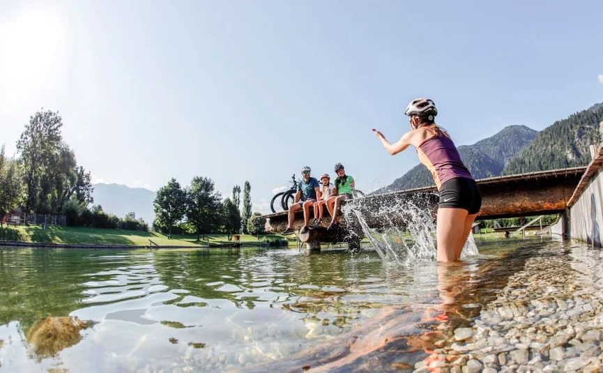 Woman splashing water in lake, three people sitting on dock with bikes
