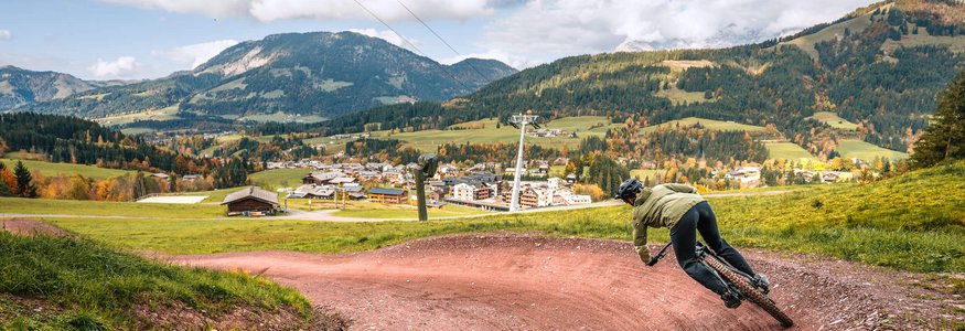 Mountain biker on winding trail with Alps and cable cars in background