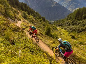 Two mountain bikers riding on a mountain trail with mountains in view