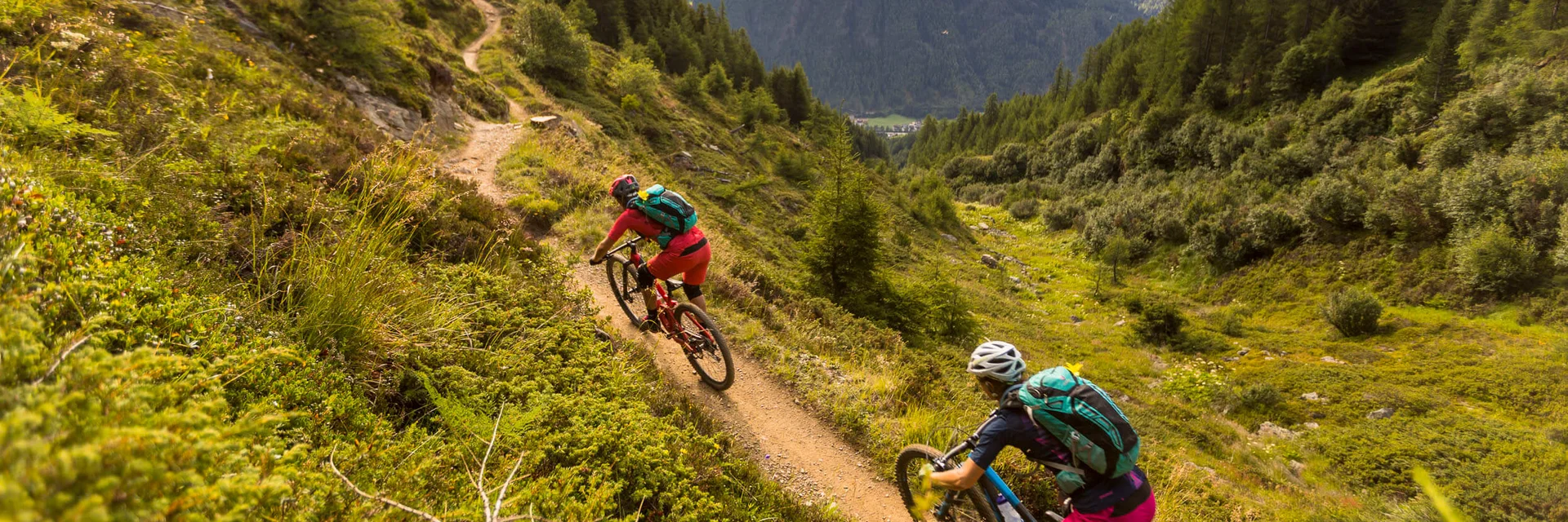 Two mountain bikers riding on a mountain trail with mountains in view