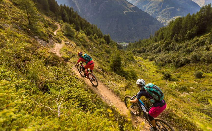 Zwei Mountainbiker fahren auf einem Bergpfad mit Bergen im Hintergrund