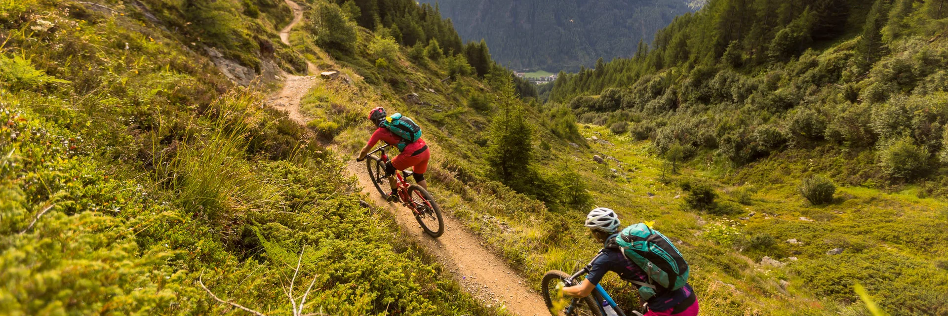 Zwei Mountainbiker fahren auf einem Bergpfad mit Bergen im Hintergrund