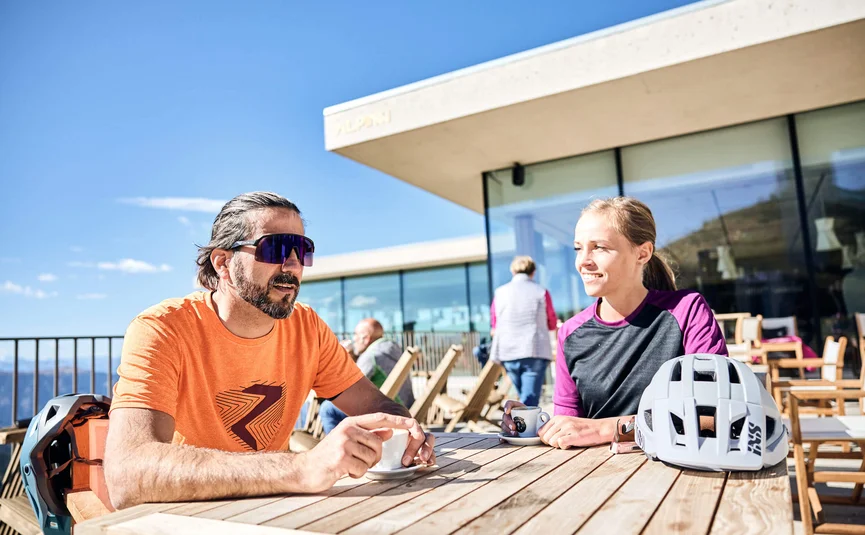 Zwei Radfahrer trinken Kaffee auf Terrasse bei sonnigem Wetter