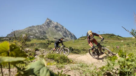 Zwei Mountainbiker fahren auf einem Bergweg mit Berg im Hintergrund