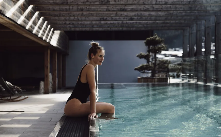 Vrouw in zwarte badpak zit aan de rand van een zwembad in een moderne ruimte
