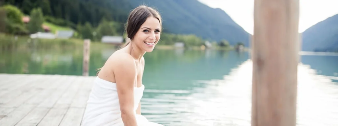 Bewusst Frau Sein Lächelnde Frau im weißen Kleid auf einem Steg an einem Bergsee