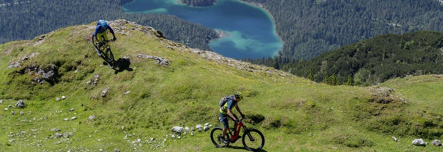 Sporthotel Schönruh **** © Bernd Ritschel Two mountain bikers riding on a grassy mountain slope with lake and forest below