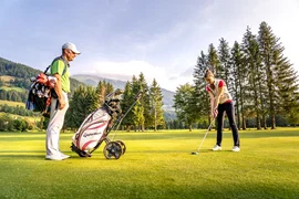 Man and woman playing golf on a green course with mountains in the background