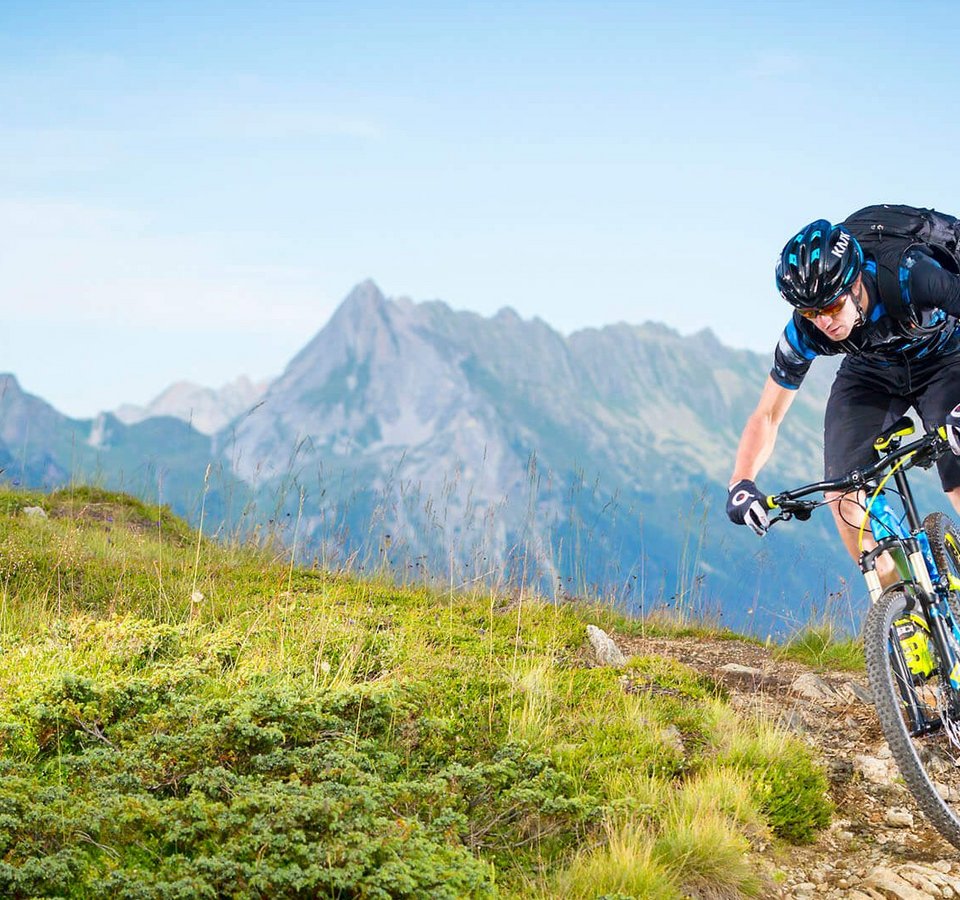 Mountainbiker fährt auf Gebirgspfad mit Alpen im Hintergrund