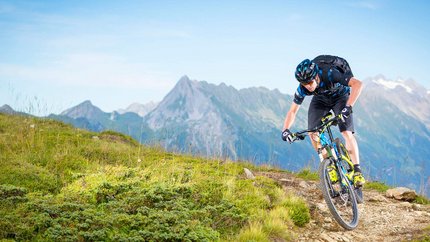 Mountainbiker fährt auf Gebirgspfad mit Alpen im Hintergrund