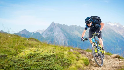Mountainbiker fährt auf Gebirgspfad mit Alpen im Hintergrund