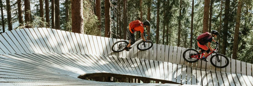 Zwei Mountainbiker fahren auf einer Holzrampe im Wald
