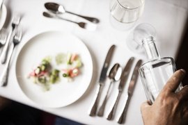 SKI + LOVE Hand holding clear bottle at set table with cutlery and small plated dish