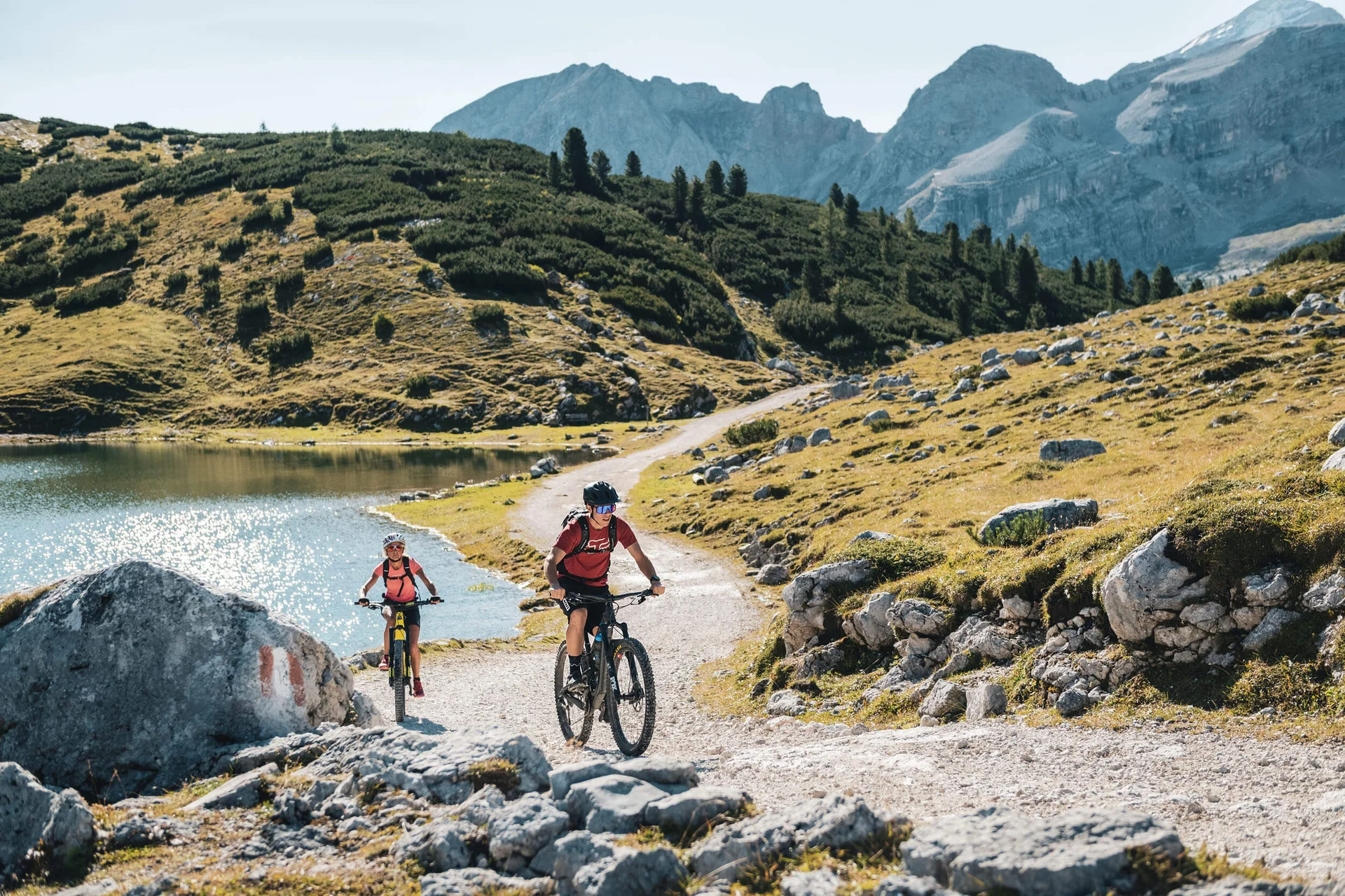 Zwei Mountainbiker fahren auf einem bergigen Wanderweg neben einem See