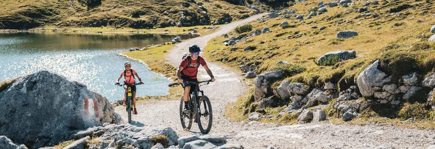 Zwei Mountainbiker fahren auf einem bergigen Wanderweg neben einem See
