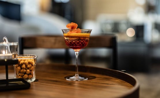 Cocktailglas mit oranger Garnitur auf rundem Holztisch in gemütlicher Umgebung