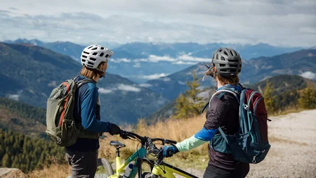 7 Highlights im NOCKBIKE-MTB-Urlaub © David Karg Zwei Radfahrer mit Helmen und Rucksäcken am Berg mit Blick auf das Tal