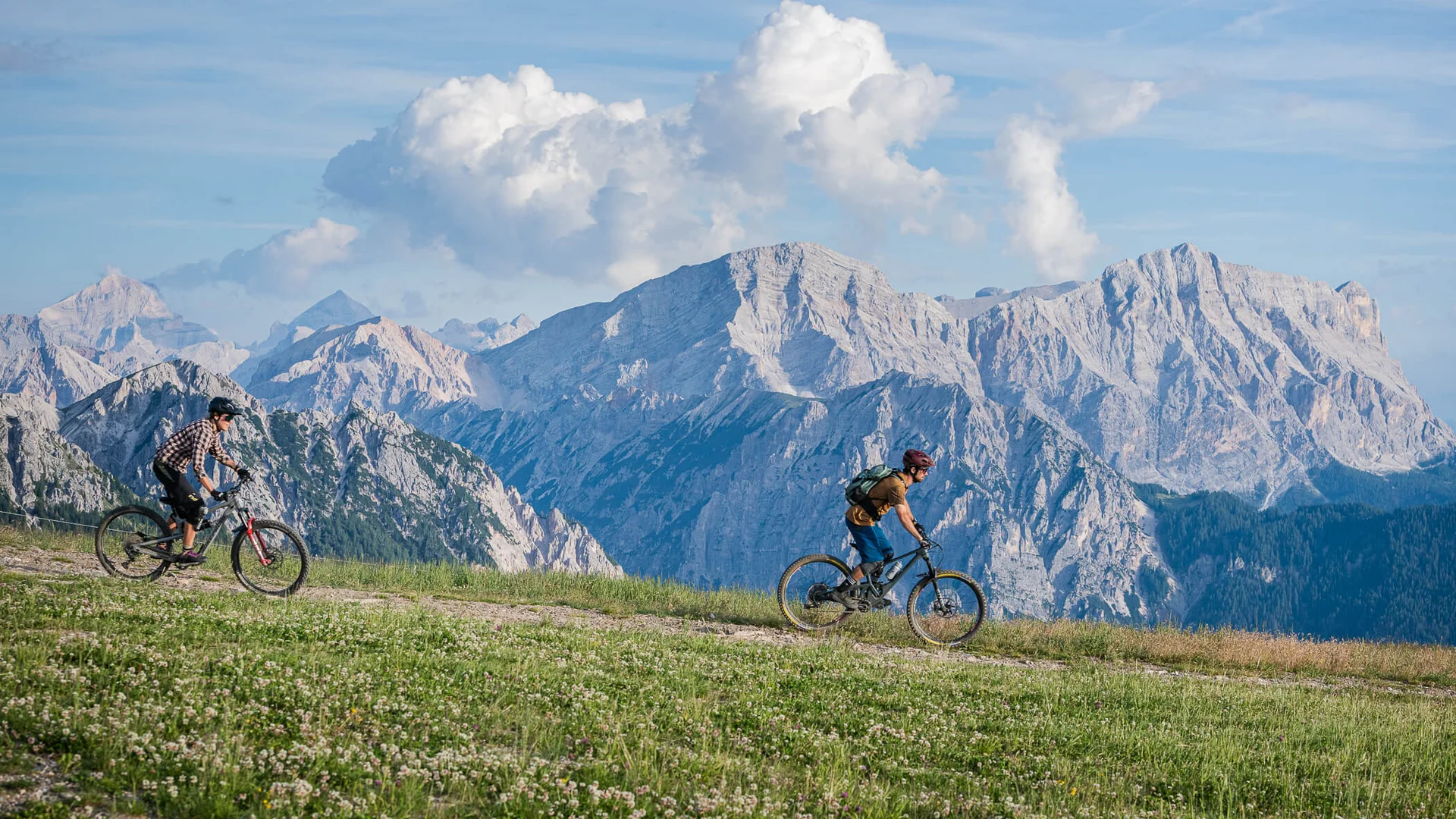 Zwei Mountainbiker fahren auf einem Bergweg mit Alpen im Hintergrund