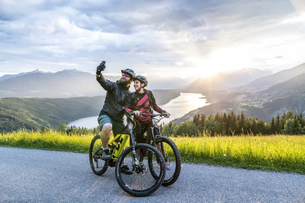 Zwei Radfahrer machen Selfie mit Berg- und Seelandschaft bei Sonnenuntergang