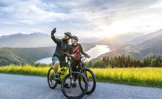 Zwei Radfahrer machen Selfie auf Bergstraße mit See und Sonnenuntergang