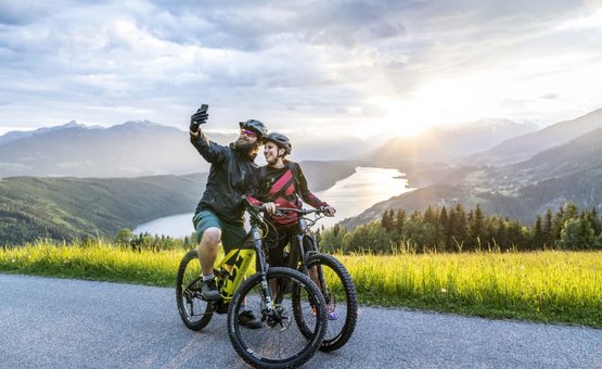 Relax und Aktiv Tage Twee fietsers maken selfie op bergweg met meer en zonsondergang