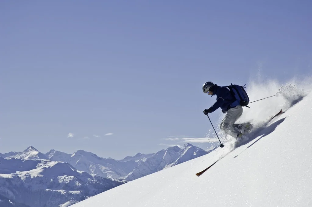 Skiër daalt een besneeuwde helling af met een berglandschap op de achtergrond