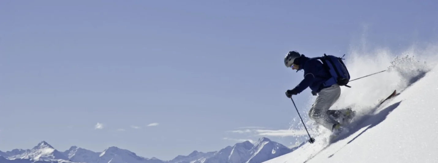 Schnee(s)pass 1-7+6 Skiër daalt een besneeuwde helling af met een berglandschap op de achtergrond
