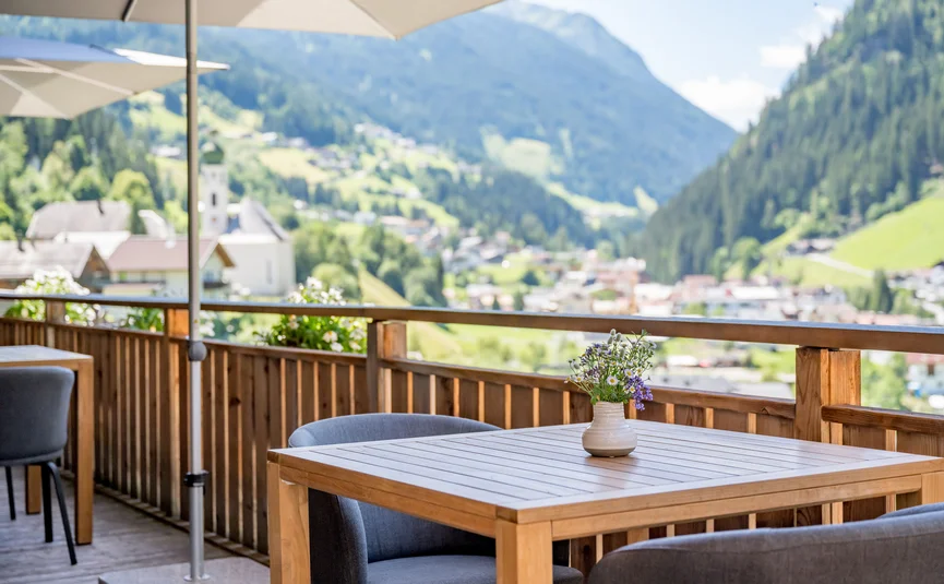 Holztisch mit Blumen auf Terrasse mit Bergblick in sonnigem Tag