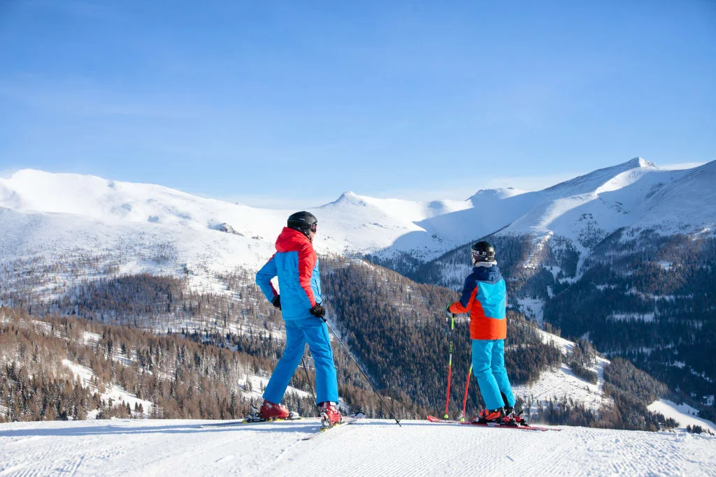 Winter Opening / 4 Nächte Twee skiërs kijken uit over besneeuwde bergen bij een heldere lucht