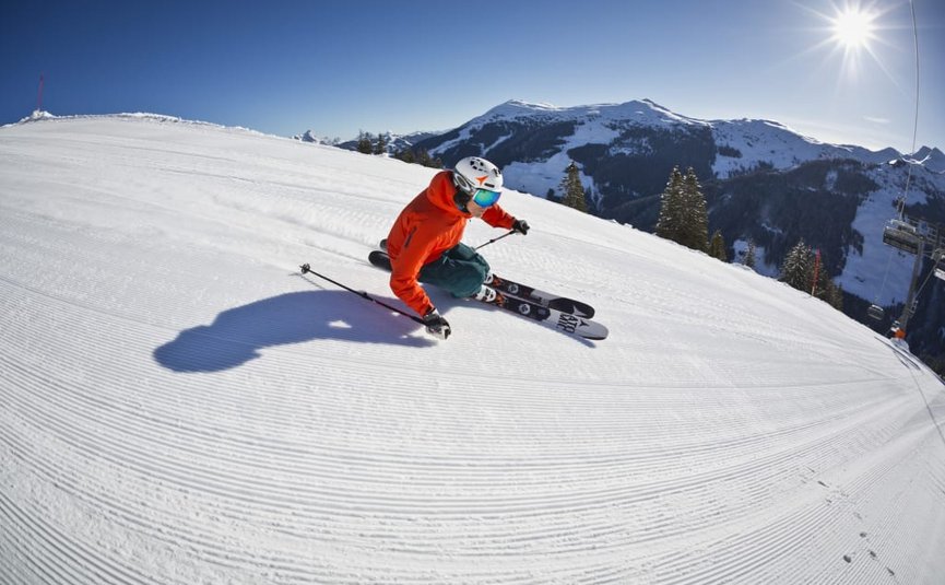 Skieën in rode jas op geprepareerde piste bij zonnig weer