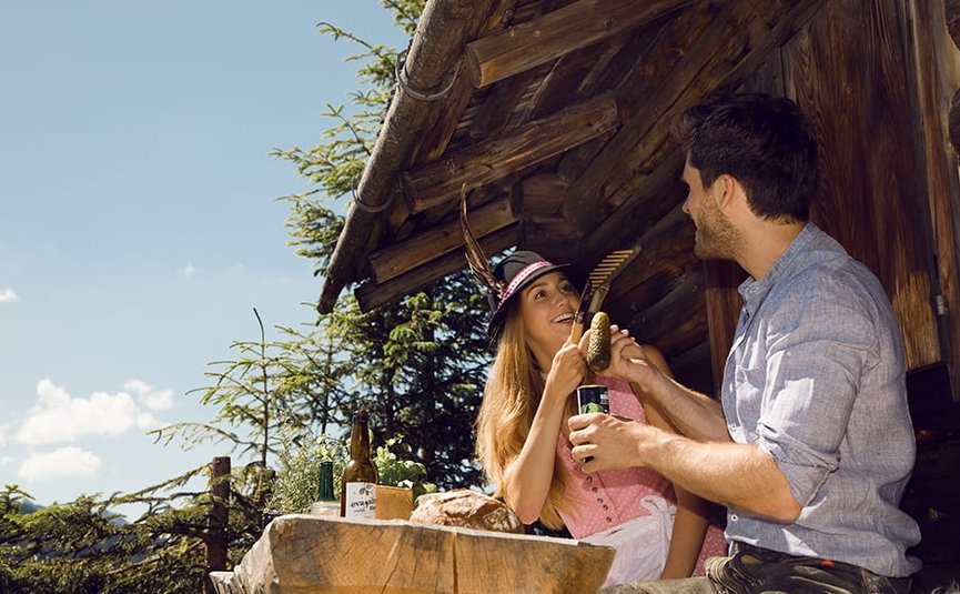 Couple in traditional clothes having a picnic outside wooden cabin in sunlight