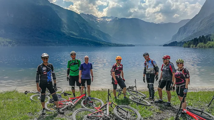 Groep fietsers bij een meer met bergen op de achtergrond onder een bewolkte lucht